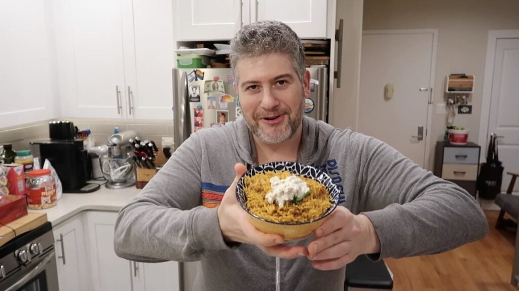 Man holding bowl of Chicken Biryani topped with cilantro and dill pickle dip